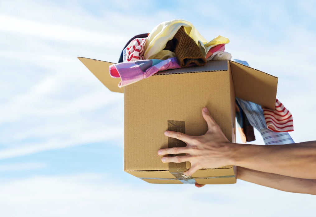 A cardboard moving box overflowing with folded, hand-me-down clothes, symbolizing inherited family patterns and programming.